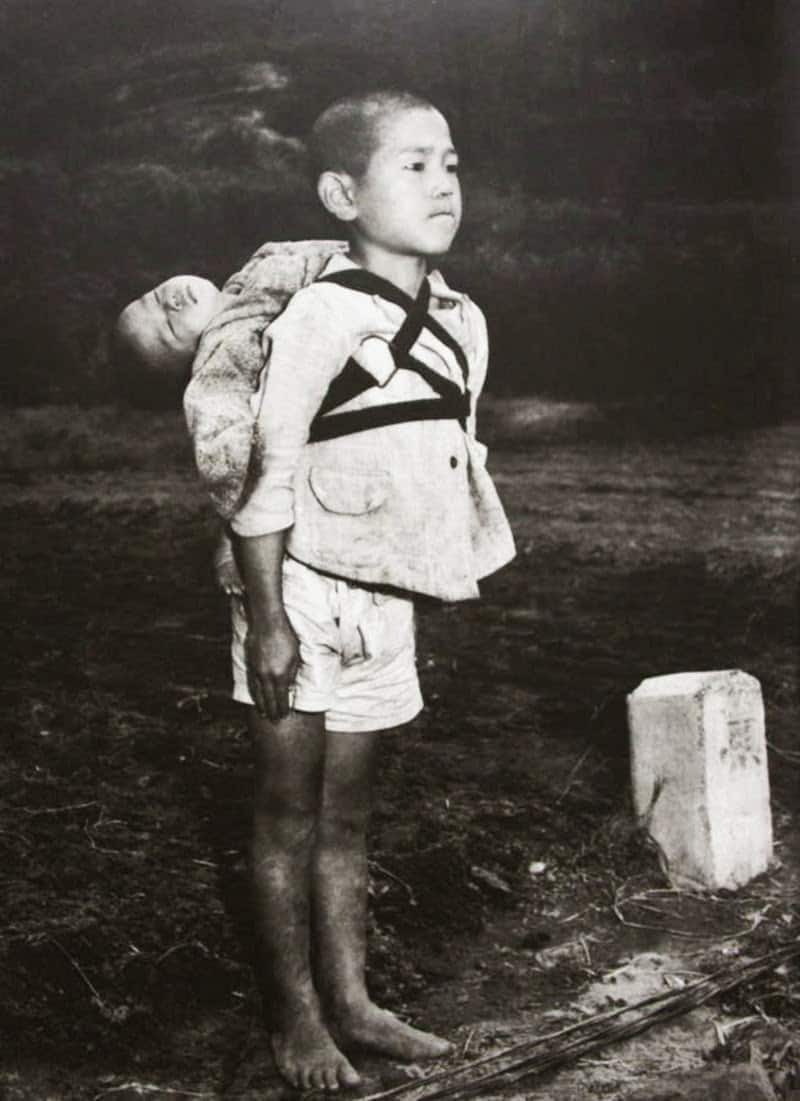 A Japanese boy standing at attention after having brought his dead younger brother to a cremation pyre, 1945 yaponaz